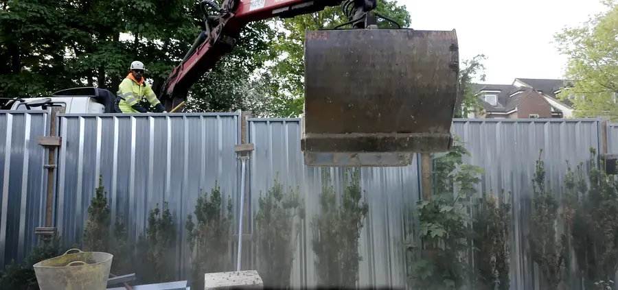 Lorry-mounted crane lifting materials over site hoarding