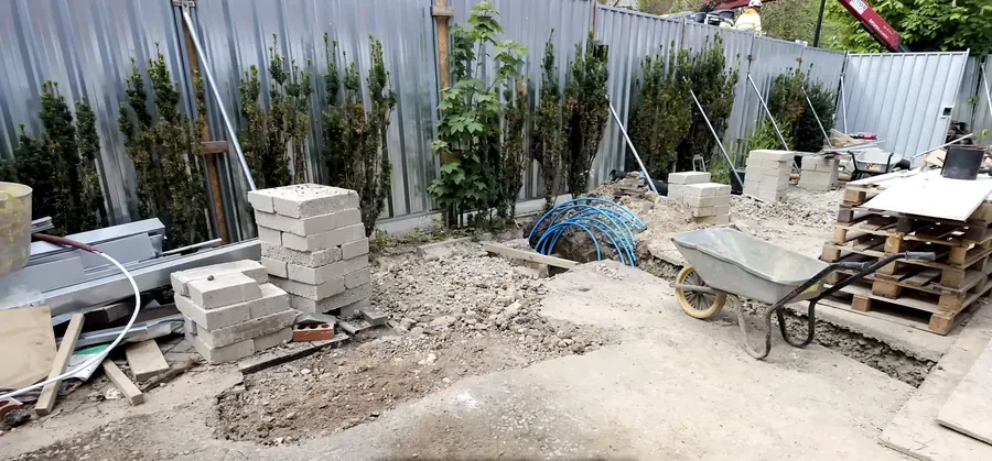 Utility works area behind site hoarding with blocks, blue duct coils and a wheelbarrow