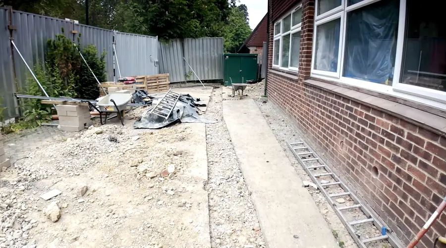 Reinstated utility trench running along a building, with materials staged on site