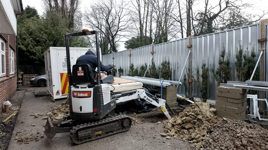 Mini excavator working on a utility connection site behind hoarding