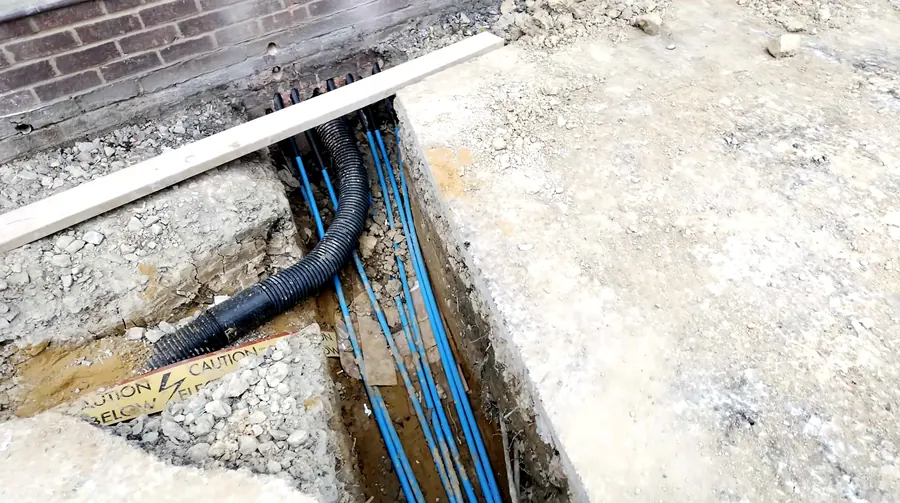 Blue water ducts and a black protective duct laid in a trench alongside a building
